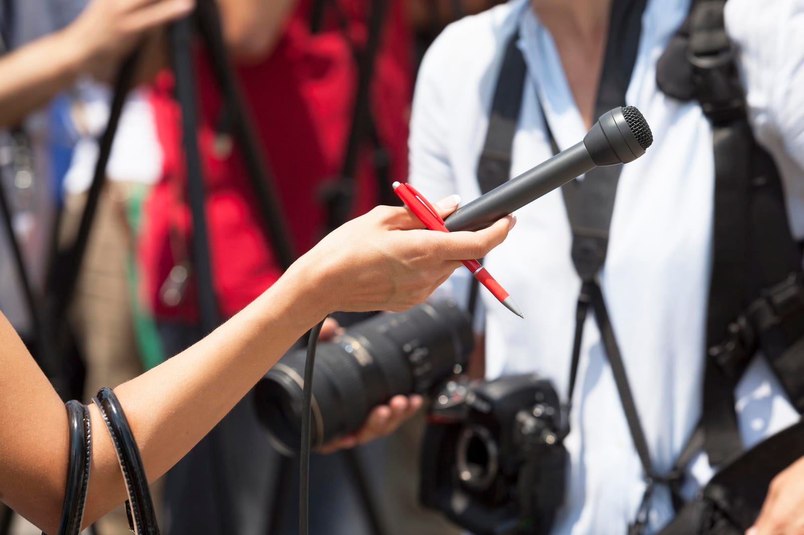 A close view of a hand holding a microphone alongside a notebook and pen at a reporting desk